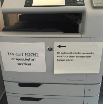 Drucker an dem zwei Zettel hängen. Auf dem ersten steht in Comic Sans: "Ich darf NICHT ausgeschaltet werden". auf dem zweiten steht mit Pfeil auf den ersten: "Ich darf kein Comic Sans verwenden wenn ich einem internationalen Konzern arbeite"